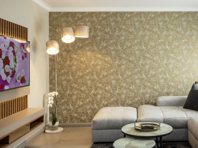 A well-appointed living room featuring a modern built-in media console, decorative wood slat wall paneling, and a stylish gold-toned patterned feature wall.