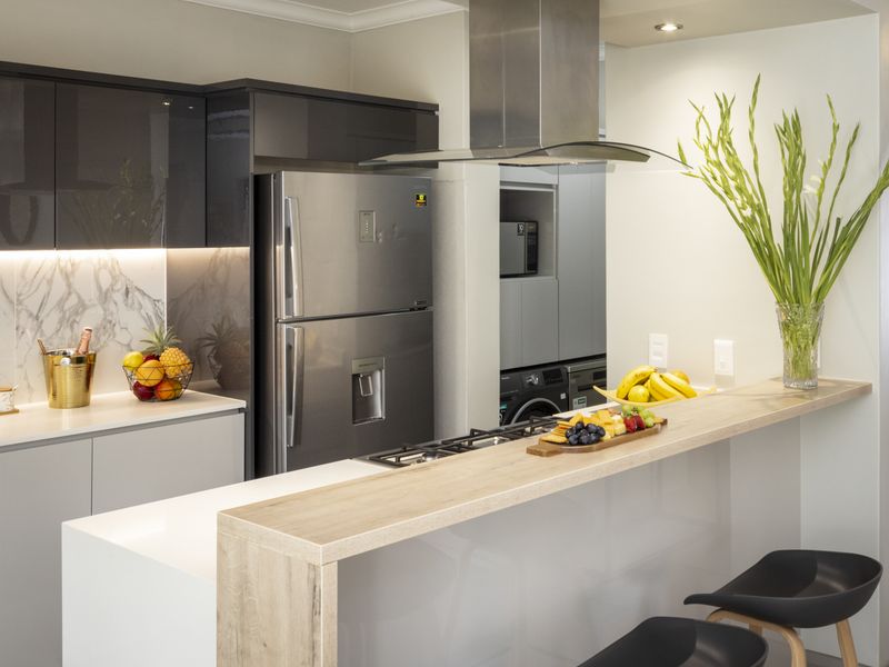 Modern kitchen featuring sleek dark cabinetry, stone countertops, a marble-look splashback, integrated gas hob, and a functional breakfast bar.