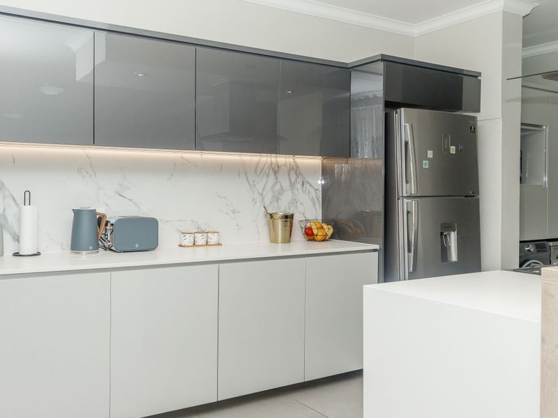 Modern kitchen featuring sleek glossy grey cabinetry, marble-look splashback, stone countertops, and integrated lighting, creating a clean and contemporary aesthetic.