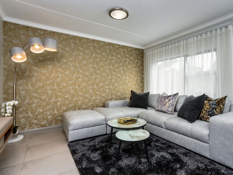 A well-maintained living room featuring tiled flooring, a decorative feature wall, and large windows with installed curtain tracks.