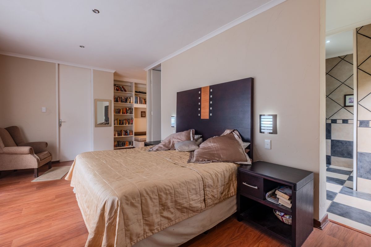 Spacious bedroom featuring laminate flooring, built-in shelving, and an adjoining bathroom with tiled finishes.