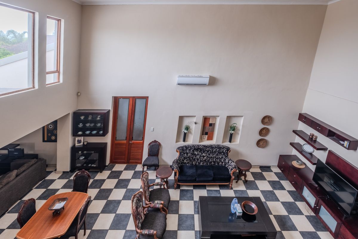 Spacious double-volume living area featuring high ceilings, checkerboard tiled flooring, built-in wall niches, and a wall-mounted air conditioning unit.