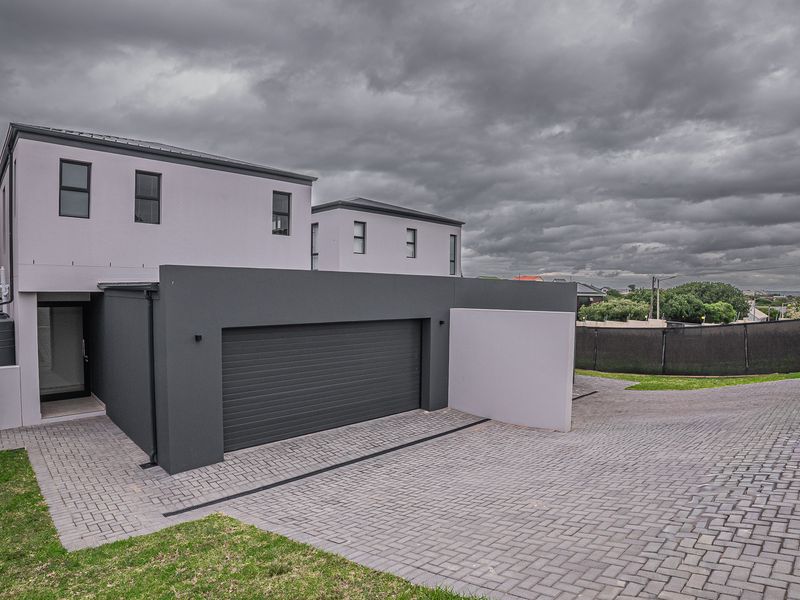 Modern townhouse exterior featuring a paved driveway, double garage with roller door, and integrated water tank, showcasing a contemporary architectural design.
