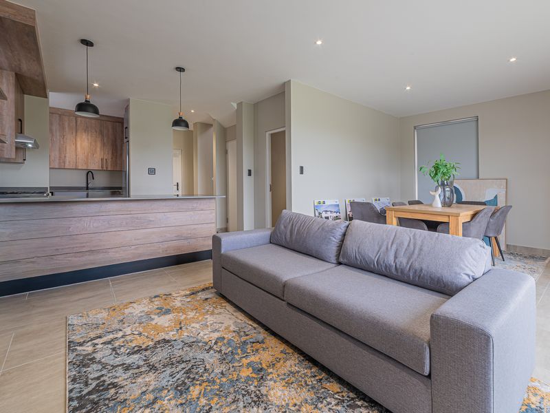Modern open-plan living area featuring a contemporary kitchen with island, sleek cabinetry, and neutral tiled flooring throughout the combined dining and lounge space.