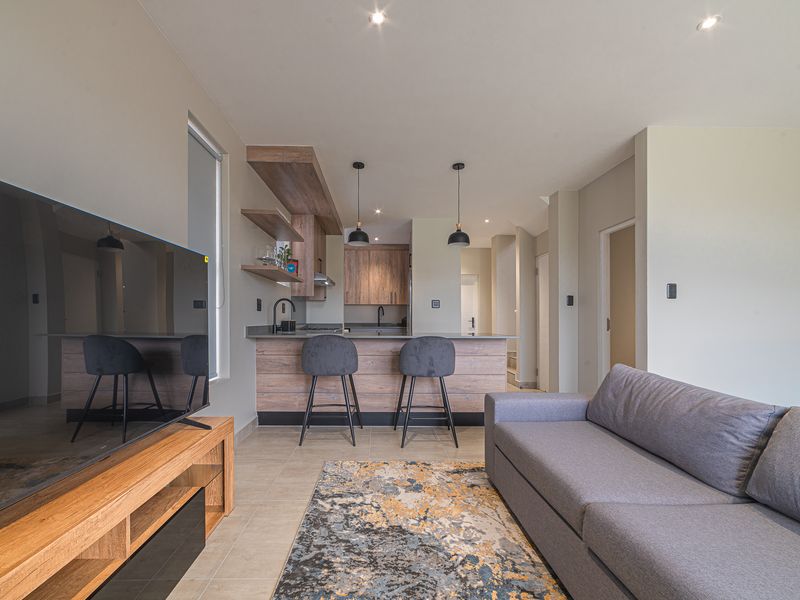 Modern open-plan living area featuring a contemporary kitchen with wood-finish cabinetry, a breakfast bar island, and neutral tiled flooring throughout.