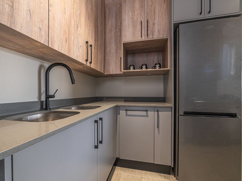 Modern kitchen featuring sleek grey cabinetry, wood-tone upper cabinets, stone countertops, and a contemporary matte black faucet.