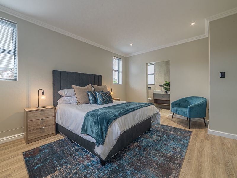 A well-maintained bedroom featuring modern laminate flooring, recessed downlighting, decorative cornicing, and direct access to an en-suite bathroom.