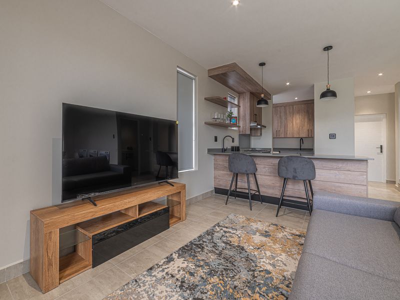 Modern open-plan living area featuring a contemporary kitchen with wood-finish cabinetry, stone countertops, breakfast bar, and integrated lighting, seamlessly flowing into the living space.