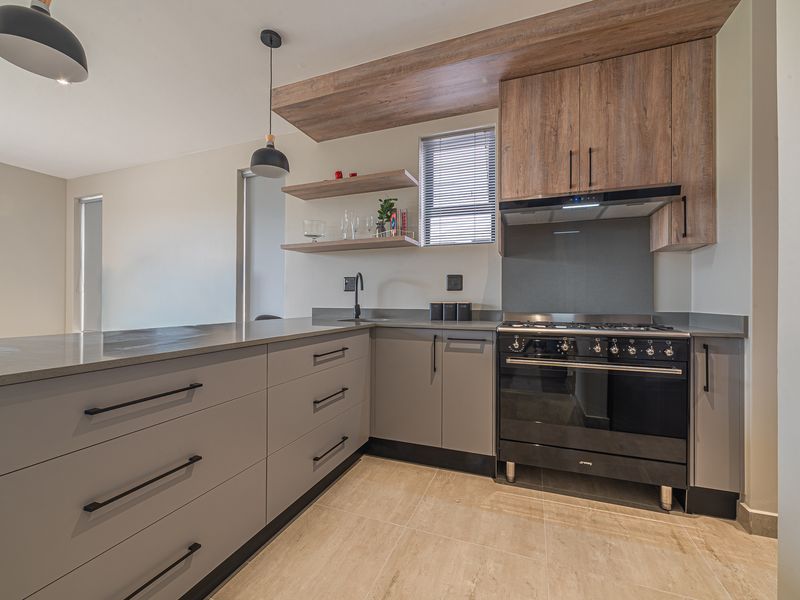 Modern kitchen featuring sleek grey cabinetry, stone countertops, floating timber shelves, and a high-quality black gas stove with integrated extractor fan.