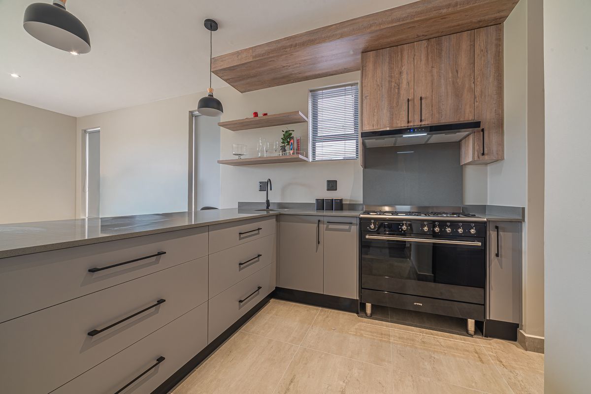 Modern kitchen featuring sleek grey cabinetry, stone countertops, floating timber shelves, and a high-quality black gas stove with integrated extractor fan.