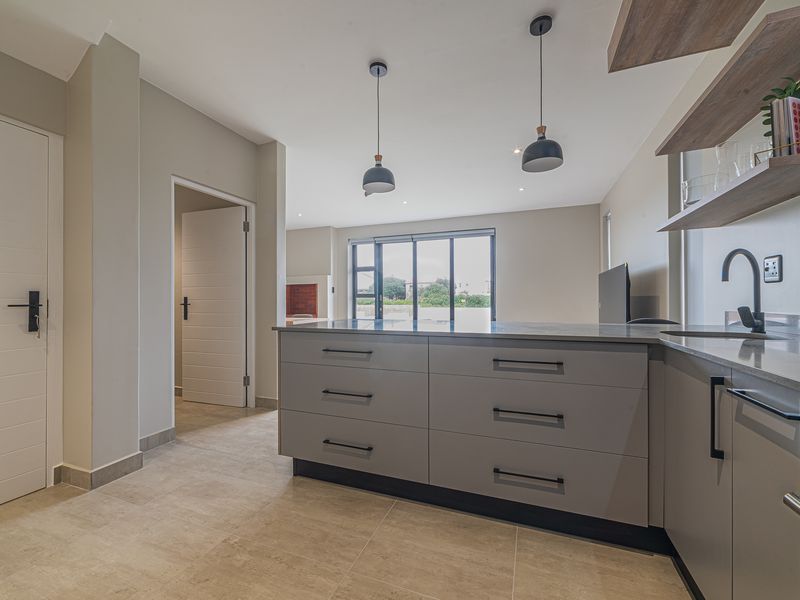 Modern open-plan kitchen featuring sleek grey cabinetry, stone countertops, built-in oven, and stylish pendant lighting, seamlessly flowing into the living area.