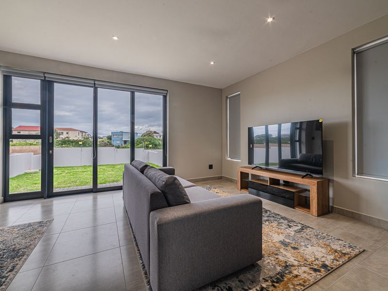 Modern living room featuring large sliding glass doors that open to a private garden, tiled flooring, and recessed downlighting.