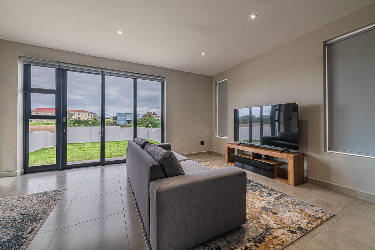 Modern living room featuring large sliding glass doors that open to a private garden, tiled flooring, and recessed downlighting.