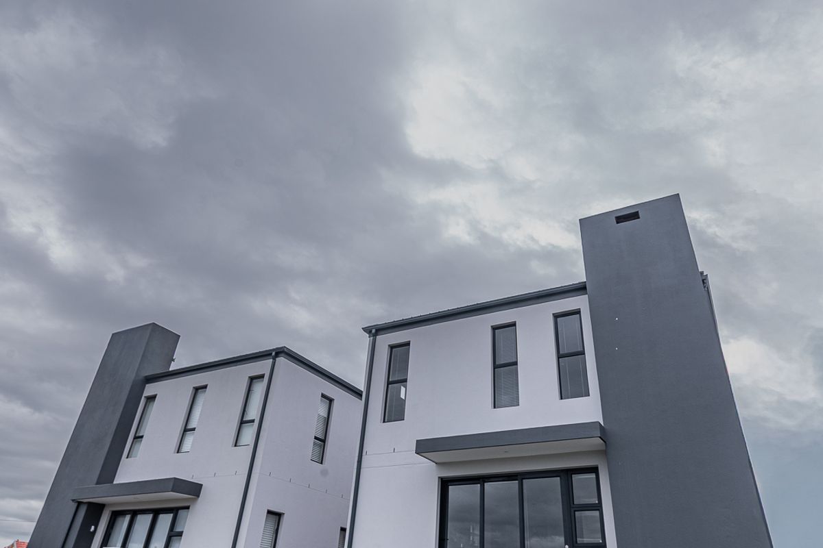 Rear view of modern double-story townhouse units featuring contemporary grey and white facade, large sliding glass doors, and a private lawn area.