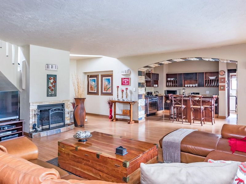Spacious open-plan living area featuring a stone-surround fireplace, laminate flooring, and a connected kitchen with a breakfast bar and built-in cabinetry.