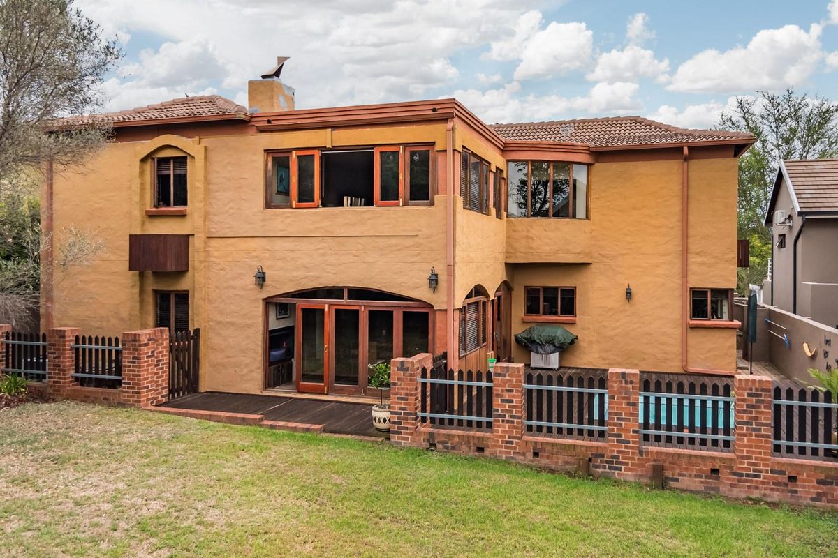 Rear elevation of a two-story house featuring terracotta roof tiles, timber-framed windows and doors, a timber deck, and a brick-enclosed garden area.