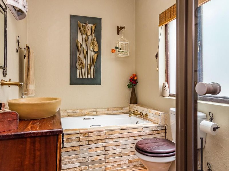 A compact bathroom featuring a stone-clad built-in bathtub, a vessel sink with wall-mounted brass faucet, and a toilet.
