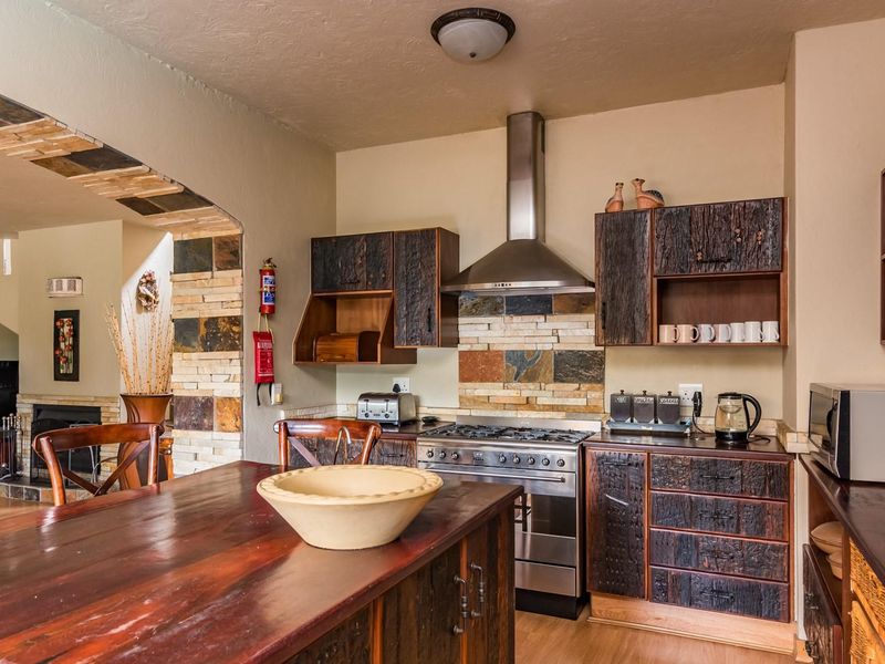 A rustic-style kitchen featuring custom timber cabinetry, a stone tile backsplash, a stainless steel gas stove, and a central timber island bench.