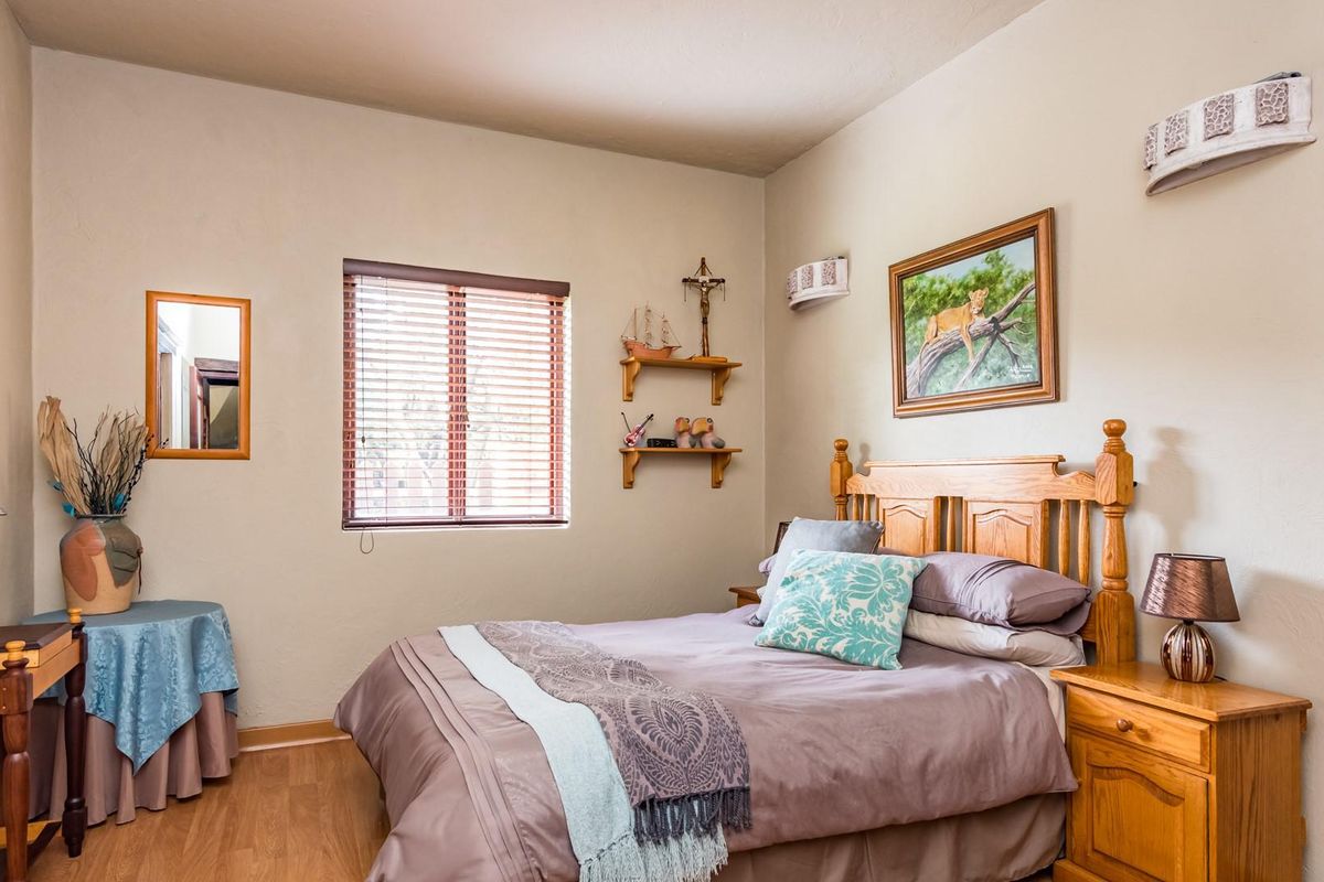 A well-maintained bedroom featuring laminate flooring, a window with fitted blinds, and wall-mounted lighting, offering a comfortable and functional living space.