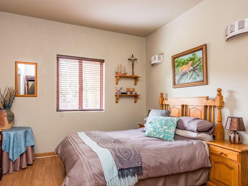 A well-maintained bedroom featuring laminate flooring, a window with fitted blinds, and wall-mounted lighting, offering a comfortable and functional living space.