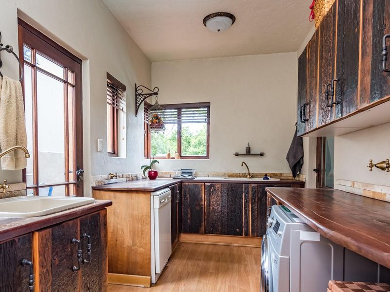 A rustic-style laundry room featuring custom dark wood cabinetry, solid wood countertops, brass hardware, and integrated appliance space with direct outdoor access.