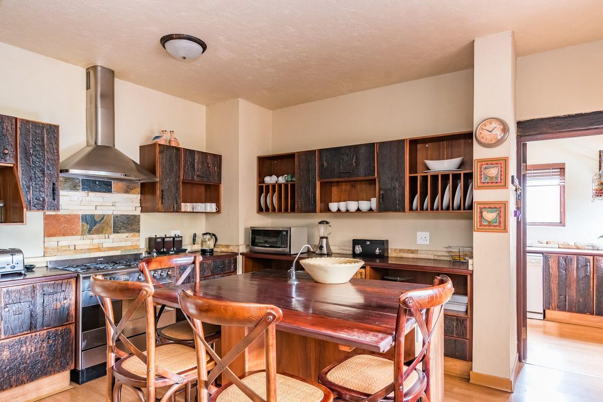 A rustic-style kitchen featuring dark textured wooden cabinetry, a stone tile backsplash, stainless steel extractor fan, and a central wooden island with integrated sink.