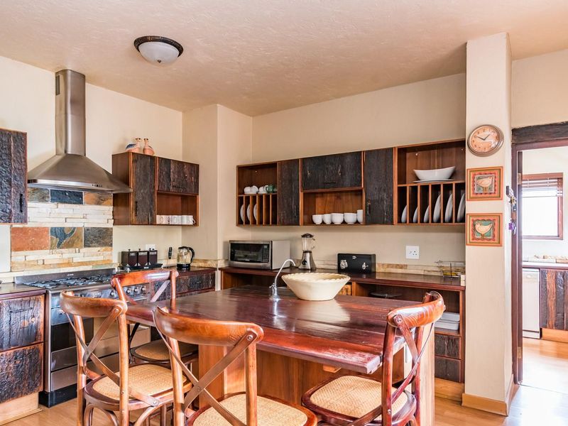 A rustic-style kitchen featuring dark textured wooden cabinetry, a stone tile backsplash, stainless steel extractor fan, and a central wooden island with integrated sink.