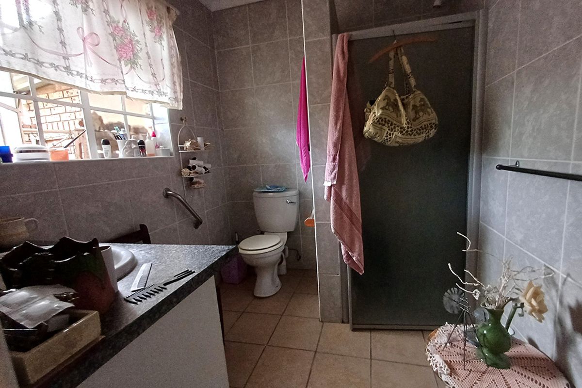 A functional bathroom featuring tiled walls and flooring, a shower enclosure, a toilet, and a vanity basin with a grab rail.