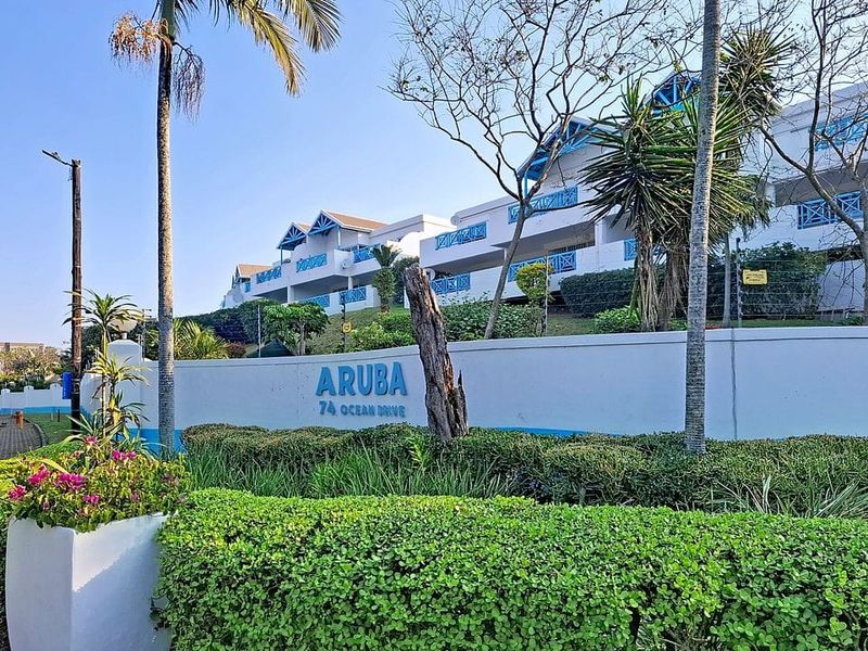 Front exterior view of the Aruba apartment complex, featuring a landscaped boundary wall and multi-story residential building facade.