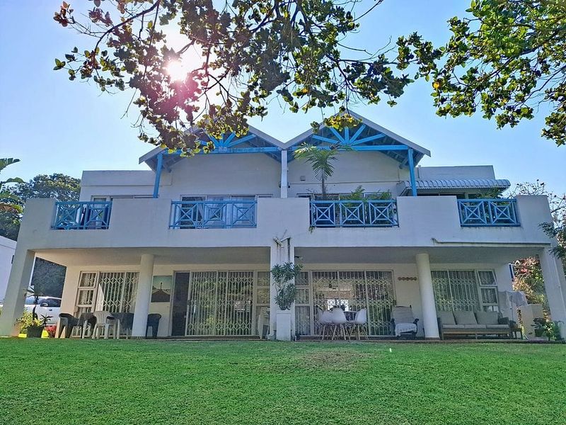 Rear elevation of a two-story apartment building featuring a ground-floor patio, upper-level balconies with blue railings, and large sliding glass doors.