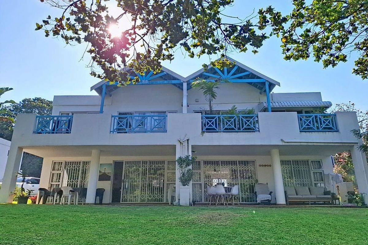Rear elevation of a two-story apartment building featuring a ground-floor patio, upper-level balconies with blue railings, and large sliding glass doors.