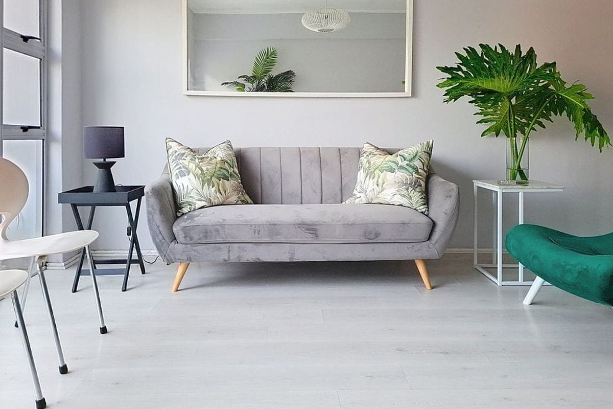 A bright and modern living room featuring light-toned laminate flooring and a large window, creating a clean and inviting atmosphere.