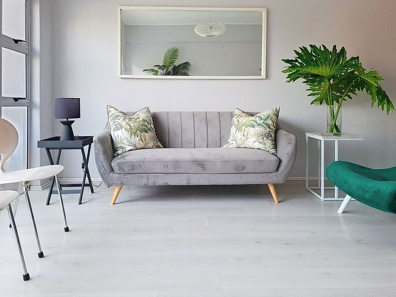 A bright and modern living room featuring light-toned laminate flooring and a large window, creating a clean and inviting atmosphere.