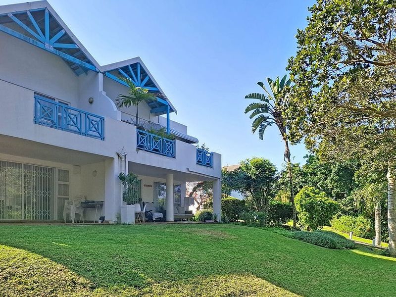 Rear view of the apartment building featuring a spacious lawn, covered ground floor patio, and upper-level balconies with blue railings.