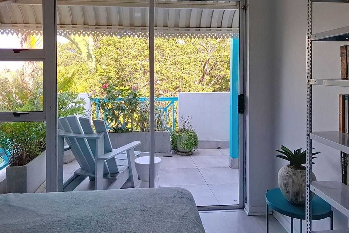 A bedroom featuring laminate flooring and a sliding glass door that opens onto a private balcony with a metal balustrade.