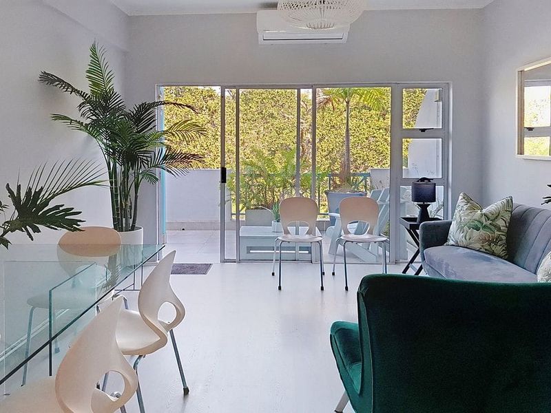 Bright open-plan living and dining area featuring modern laminate flooring, a wall-mounted air conditioner, and large sliding glass doors leading to a private balcony.
