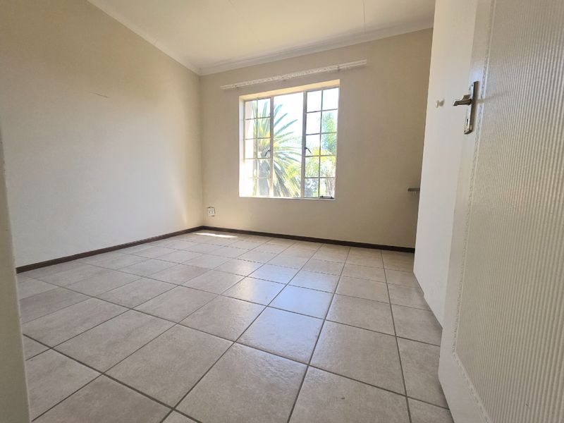A bright, empty bedroom featuring neutral tiled flooring, large windows with security bars, and clean wall finishes, ready for personalization.