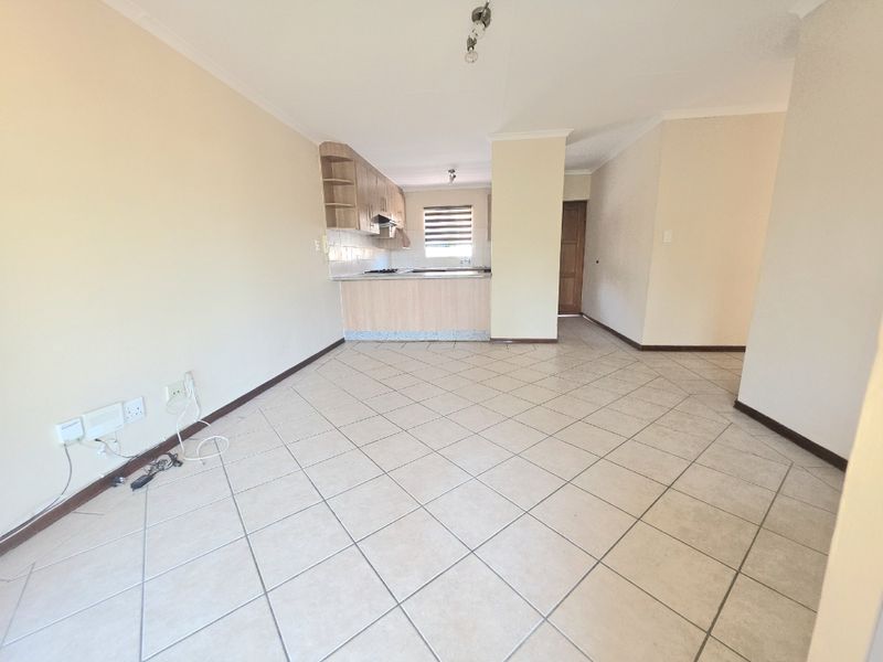 An open-plan living and kitchen area featuring tiled flooring, neutral walls, and built-in kitchen cabinetry with a functional hob and extractor fan.