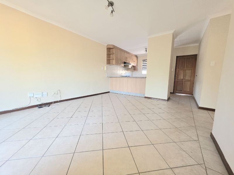 An open-plan living area featuring tiled flooring, neutral walls, and a functional kitchen with built-in cabinetry and a breakfast counter.