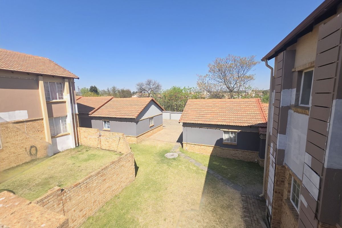 View of the rear communal garden area between apartment blocks, featuring brick boundary walls, paved pathways, and terracotta tiled roofs.
