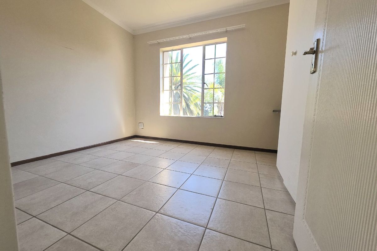 A bright, empty bedroom featuring neutral tiled flooring, large windows with security bars, and clean wall finishes, ready for personalization.