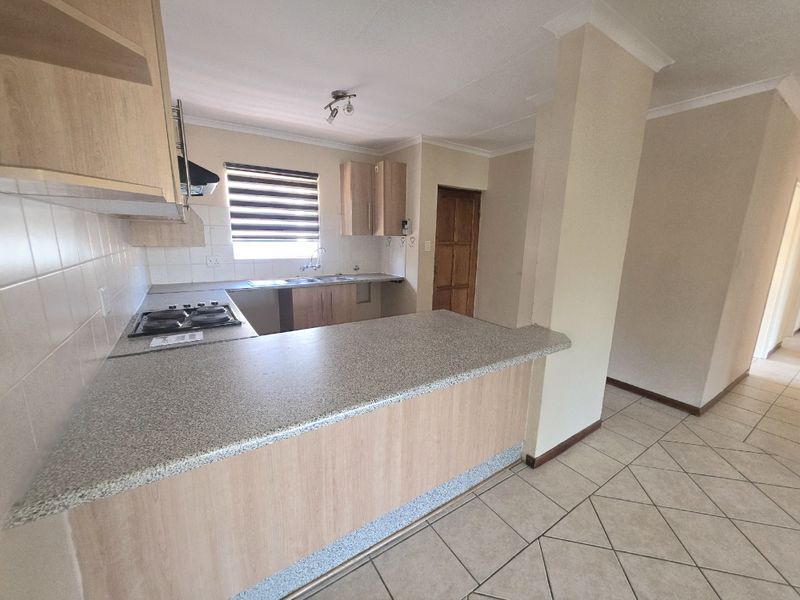 A functional kitchen featuring light wood cabinetry, laminate countertops, a gas hob with extractor, and a breakfast bar, finished with neutral tiled flooring.