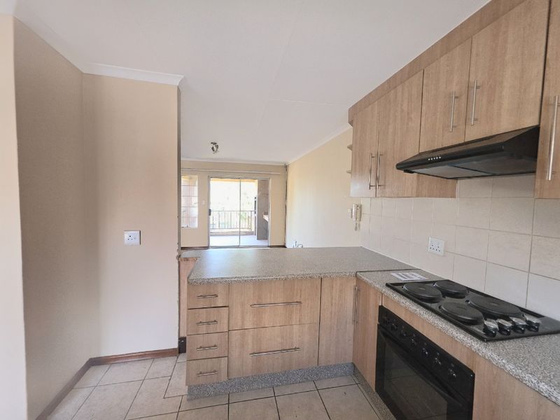 Open-plan kitchen featuring laminate cabinetry, built-in oven and hob, and tiled flooring, flowing into a living area with access to a balcony.