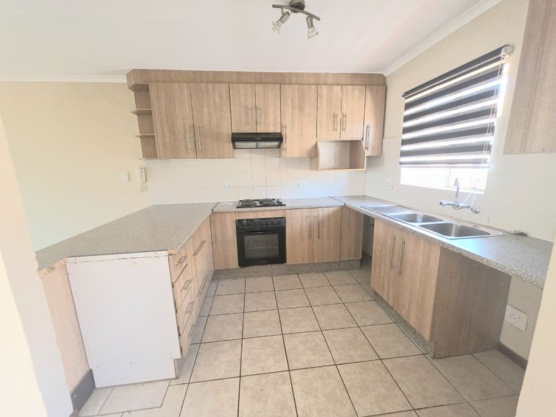 A functional kitchen featuring light wood-look cabinetry, built-in oven and hob, double sink, and tiled flooring with a neutral backsplash.