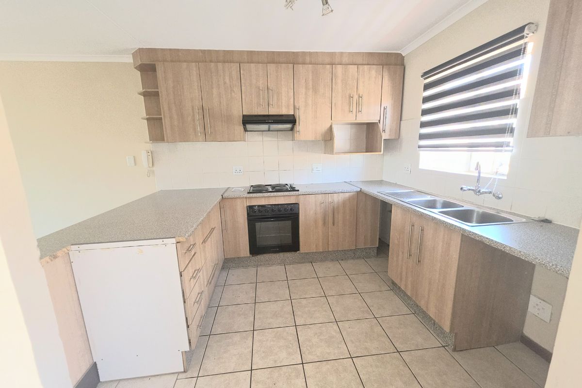 A functional kitchen featuring light wood-look cabinetry, built-in oven and hob, double sink, and tiled flooring with a neutral backsplash.