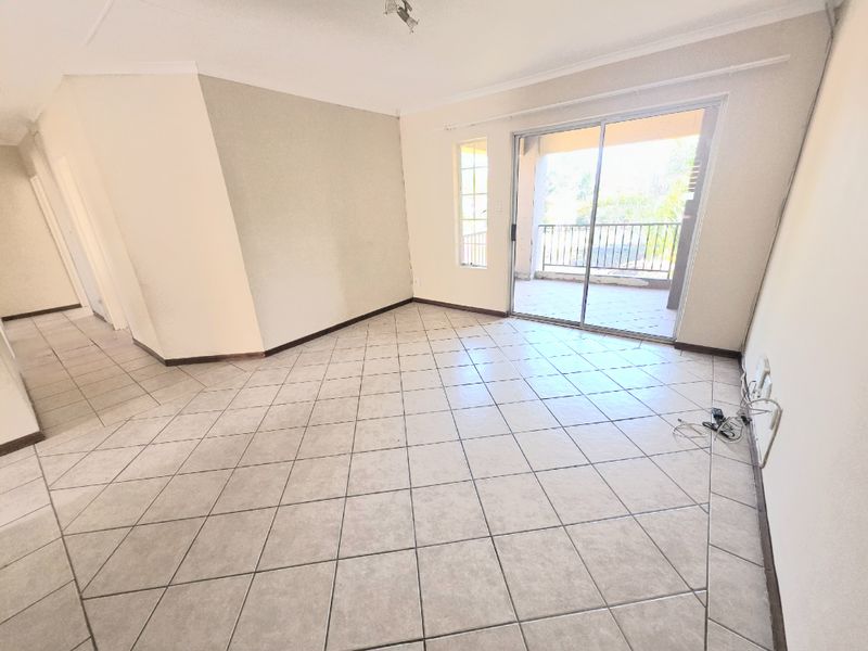 An empty living room featuring tiled flooring, neutral walls, and a sliding glass door providing direct access to an outdoor balcony.