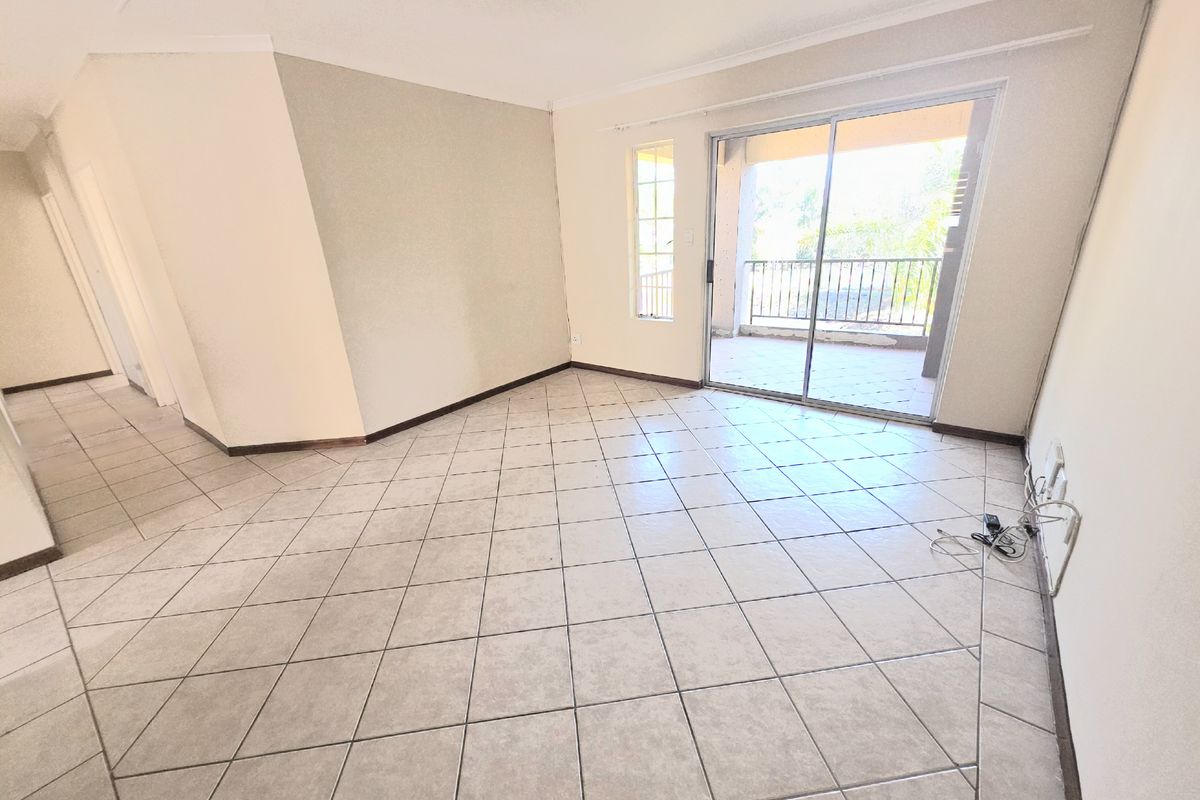 An empty living room featuring tiled flooring, neutral walls, and a sliding glass door providing direct access to an outdoor balcony.