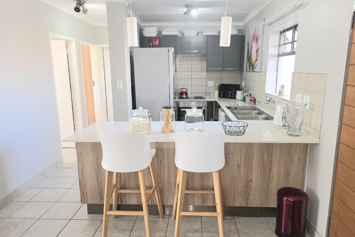 Modern kitchen featuring a central island with quartz countertops, sleek cabinetry, built-in appliances, and contemporary pendant lighting, finished with neutral tiled flooring.