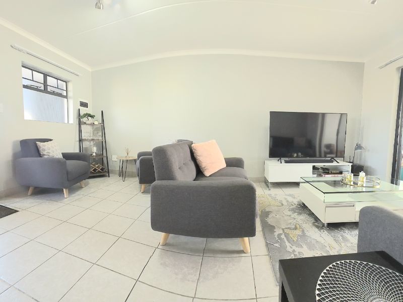 A bright and spacious living room featuring neutral tiled flooring, cove cornicing, and large sliding glass doors providing access to the outdoor area.