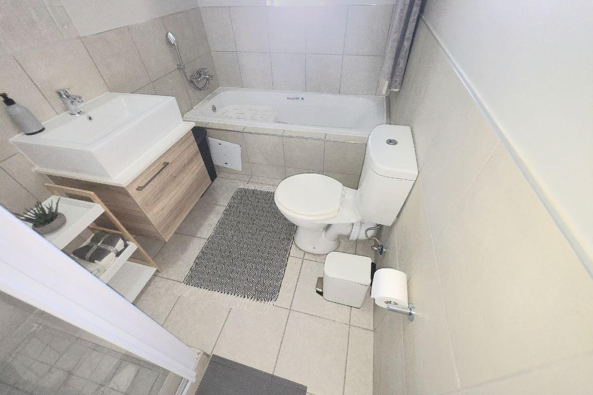A functional bathroom featuring a vanity cabinet with basin, a bathtub, and a toilet, finished with neutral wall and floor tiles.